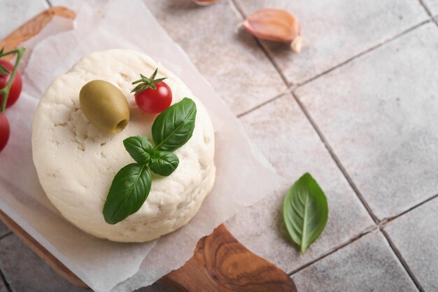 Ricotta Ricotta fatta in casa con basilico aglio pomodori e olive verdi su pergamena brossura e stand su vecchie piastrelle beige sfondo Cibo italiano Messa a fuoco selettiva