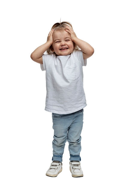 Ridere bambina 2-3 anni in jeans si alza e tiene la testa. Isolato su sfondo bianco. Verico. A tutta altezza.