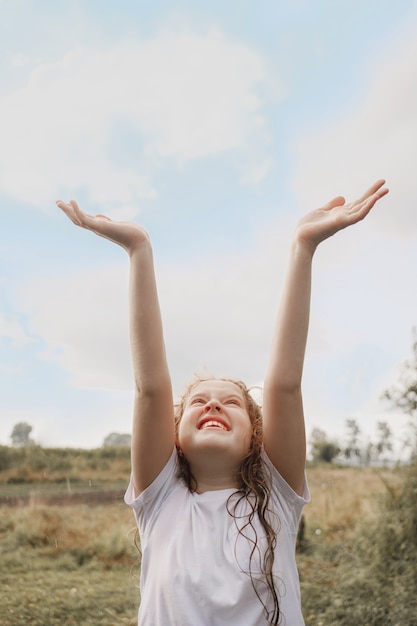 Ridere bambino allargò le braccia e cattura gocce di pioggia e raggi solari.