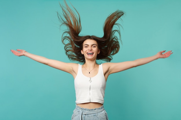 Ridere giovane donna in abiti casual leggeri allargando le mani, saltando con i capelli svolazzanti isolati su sfondo blu muro turchese. Persone sincere emozioni, concetto di stile di vita. Mock up copia spazio.