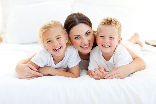 Ridere i bambini che giocano con la loro madre sdraiata su un letto