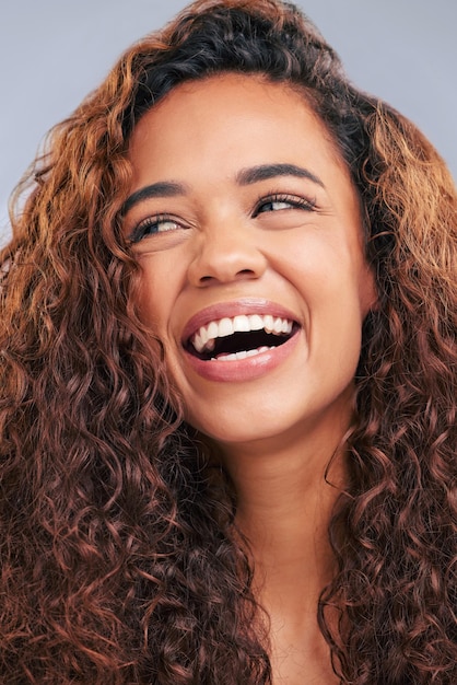 Ridere i capelli ricci e la donna naturale in studio con il sorriso e il bagliore del viso Persona di sesso femminile felice con bellezza e riccioli sani come benefici o risultati di shampoo o cosmetici su uno sfondo grigio