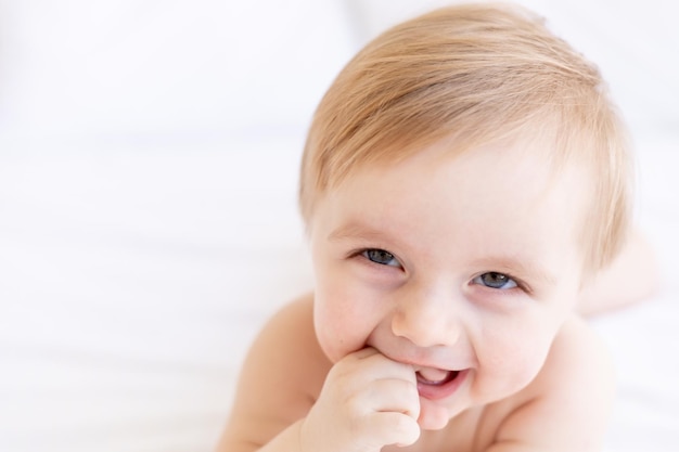 Ridere o sorridere biondo bambino con grandi occhi con un dito in bocca primo piano o ritratto in una culla a casa il concetto di articoli per bambini e accessori