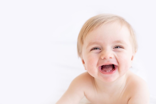 Ridere o sorridere biondo bambino con occhi grandi primo piano o ritratto in una culla a casa il concetto di beni e accessori per bambini