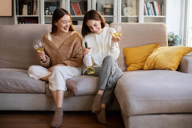 Ridere signore millenarie europee in maglioni con bicchieri di bottiglia di vino godersi il riposo rilassarsi festa nel tempo libero