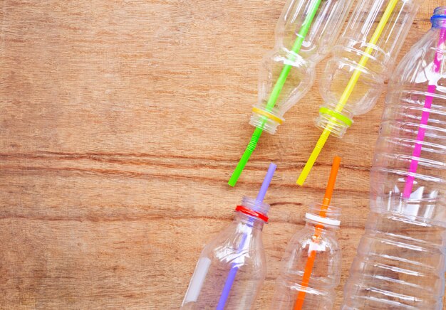 Rifiuti di plastica, bottiglie di plastica con cannucce su fondo di legno.