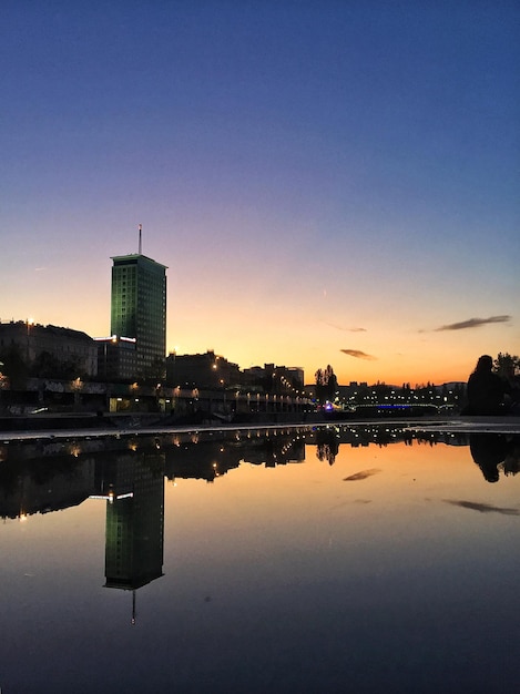 Riflessione degli edifici nel lago contro il cielo durante il tramonto