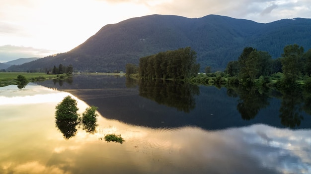 Riflessione delle montagne su un fiume durante un tramonto dorato nuvoloso