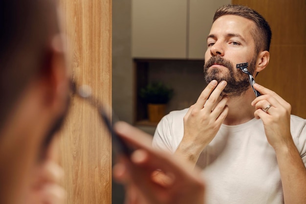 Riflessione di un uomo che si rade la barba con una lama di rasoio