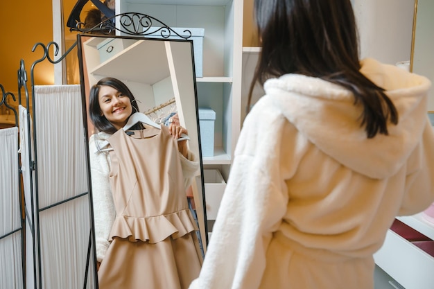 Riflessione di una giovane donna sorridente in accappatoio che sceglie un vestito davanti a uno specchio a casa o in un hotel