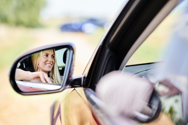 Riflessione nello specchietto retrovisore esterno della donna sorridente che guida l'auto