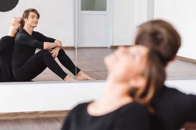 Riflessione nello specchio. Bello bel giovane ballerino seduto vicino al suo compagno di ballo e sorridente mentre si guarda allo specchio