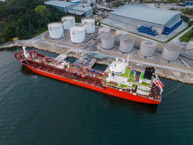 Rifornimento di carburante di una nave cisterna presso un terminal petrolifero con silos di stoccaggio nel porto, vista aerea da un drone volante