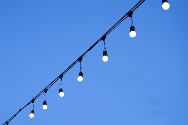 Riga della lampadina illuminata che appende sulla stringa e sul cielo blu