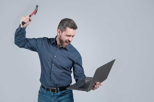 Rilasciare la rabbia sul computer. Uomo stressato che urla e rompe il computer portatile con il martello. Guasto al computer. Impatto negativo della tecnologia. Si è stressato.