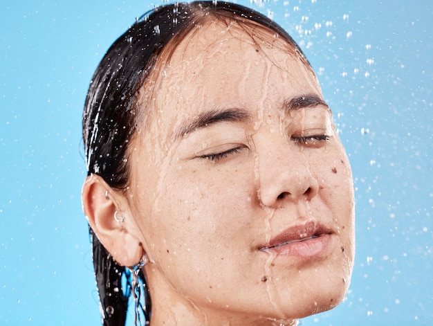 Rilassa l'acqua e il volto di una donna sotto la doccia per pulire la pace e la salute su uno sfondo blu da studio Benessere per la cura della pelle e modello asiatico con bellezza per la cura dei capelli e cura di sé naturale