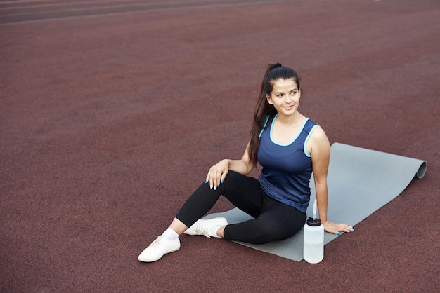 Rilassamento dopo la pratica dello yoga all'aperto Donna che riposa su un materassino da yoga seduto nello stadio