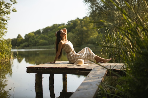 Rilassante giovane donna sul molo di legno al calmo lago