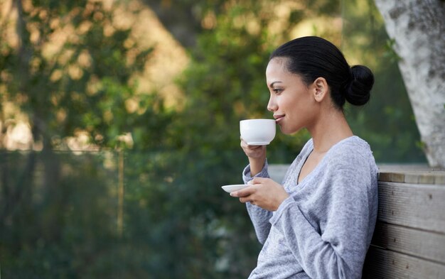 Rilassarsi con la sua bevanda preferita Foto di una giovane ragazza etnica che si gode una tazza di caffè all'esterno