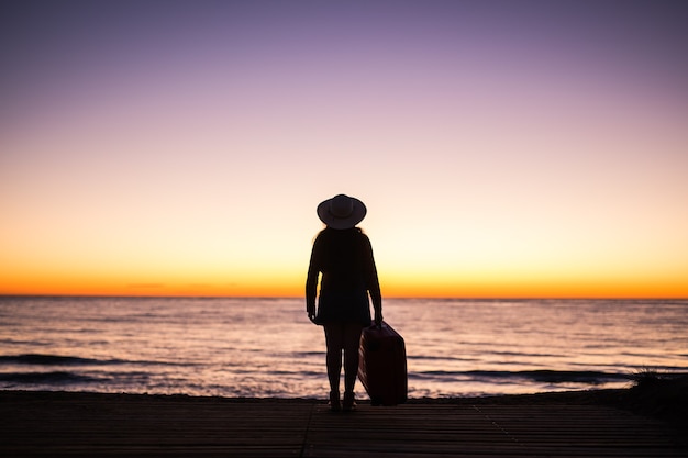 Rilassarsi donna con la valigia su una spiaggia al tramonto silhouette vacanza viaggio concetto giovane signora