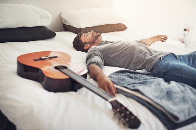 Rilassarsi dormire e l'uomo a letto con la stanchezza della chitarra e ricaricare per l'ispirazione musicale nella stanza d'albergo esausto pisolino mattutino e musicista stanco in camera da letto con la gestione del tempo per il programma di concerti