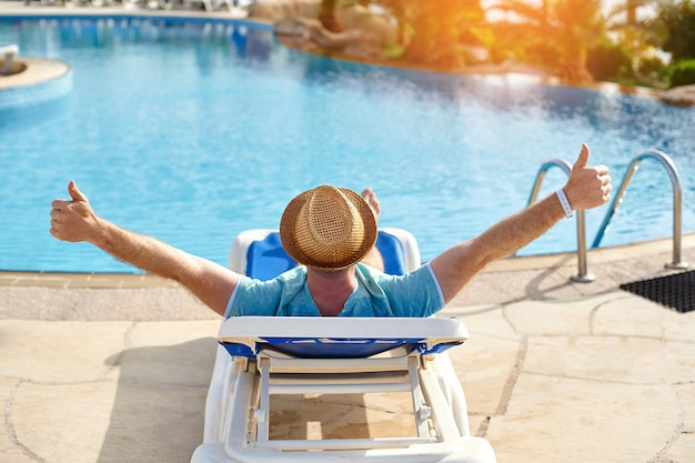 Rilassarsi in piscina estate. Uomo giovane e di successo sdraiato su un lettino in hotel sullo sfondo del tramonto