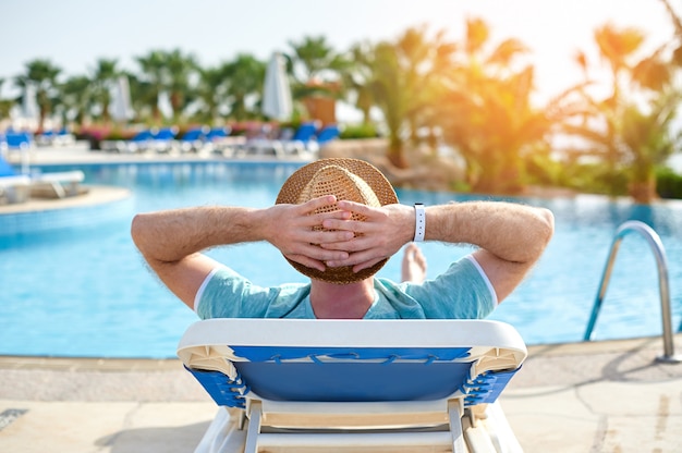 Rilassarsi in piscina estiva. Giovane e riuscito uomo che si trova su una sdraio in hotel sullo sfondo del tramonto, tempo di concetto di viaggiare