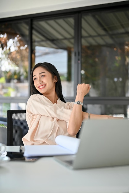 Rilassata donna d'affari asiatica millenaria che allunga le braccia prendendo una pausa dal lavoro