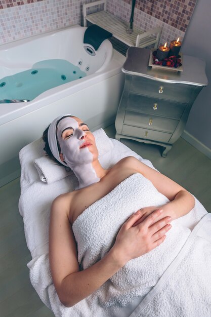 Rilassata giovane donna che riposa sdraiata con maschera facciale di argilla nella spa. Medicina, sanità e concetto di bellezza.