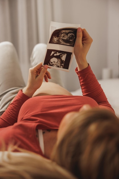 Rilassata giovane futura madre che guarda l'ecografia del suo bambino mentre si rilassa su un letto in camera da letto.