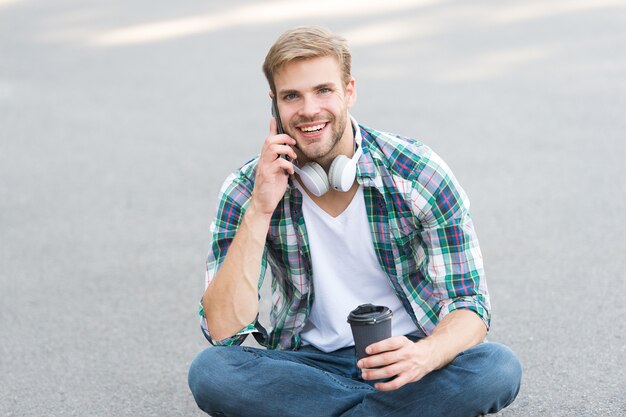 Rilassati e ricaricati. Divertiti durante la pausa. Chiama amico. Lo studente spensierato del ragazzo gode del caffè all'aperto. Equilibrio di vita. Benessere e salute. Fare una pausa caffè. L'uomo si siede a terra mentre beve il caffè.