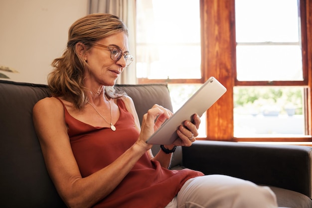 Rilassati l'e-commerce e la donna in pensione su tablet con occhiali da lettura su internet a casa in Canada Persona anziana che guarda le offerte di shopping online sull'app di vendita al dettaglio mentre si riposa sul divano del soggiorno