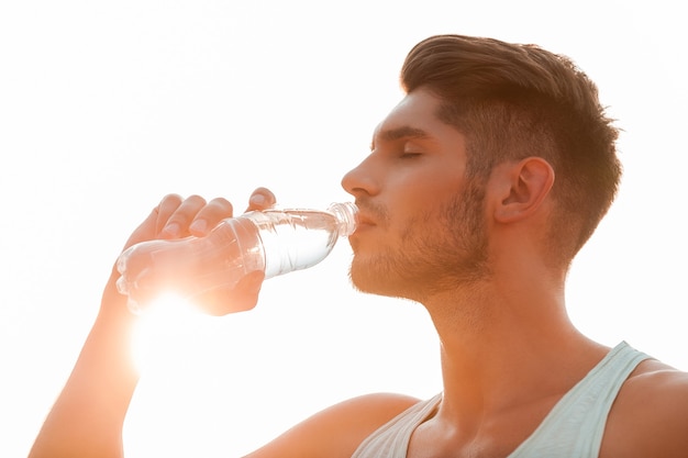 Rimanere idratati. Inquadratura dal basso del giovane che beve acqua e tiene gli occhi chiusi mentre si sta in piedi all'aperto