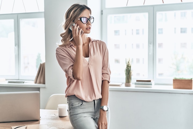 Rimanere in contatto con i colleghi. Bella giovane donna che parla al telefono cellulare mentre si trova in un ufficio moderno