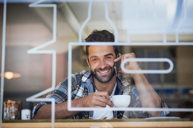 Rimanere in contatto durante la pausa caffè Ritratto di un giovane felice che risponde al cellulare mentre beve un caffè nel suo bar preferito