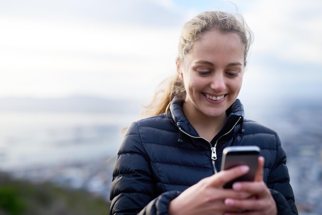 Rimanere in contatto ovunque vada Inquadratura ritagliata di una giovane donna attraente che invia messaggi al cellulare all'esterno