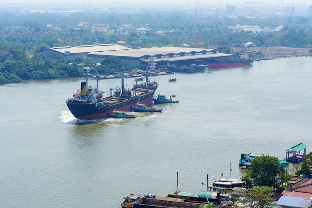 Rimorchiatori del fiume che spingono nave porta-container nel mezzo del fiume Chao Phraya
