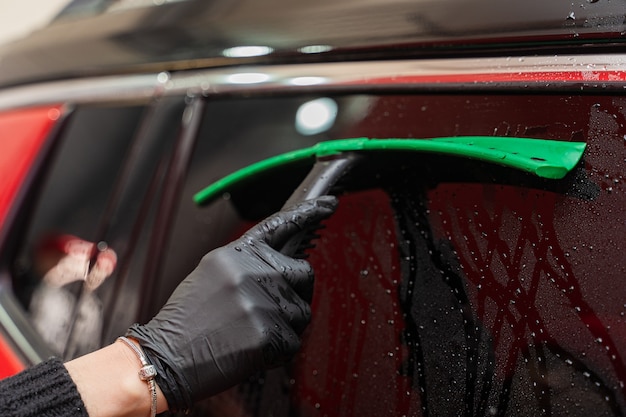Rimozione dell'acqua residua dal vetro con un raschietto in gomma dopo il lavaggio dell'auto. Autolavaggio. Complesso self-service. Autolavaggio ad alta pressione.