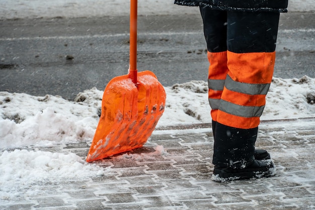 Rimuovere la neve dal marciapiede dopo la tempesta di neve Un lavoratore stradale con una pala in mano e in abiti speciali pulisce il marciapiede e la strada dalla neve Tempesta di neve e uragano in città