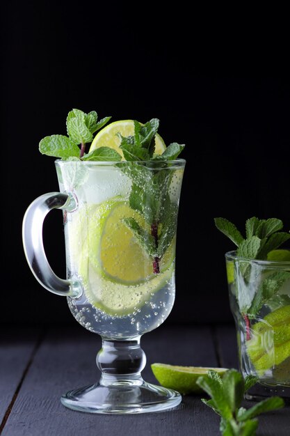 Rinfrescante mojito freddo in un bicchiere alto con ghiaccio menta limone e lime su sfondo nero Primo piano