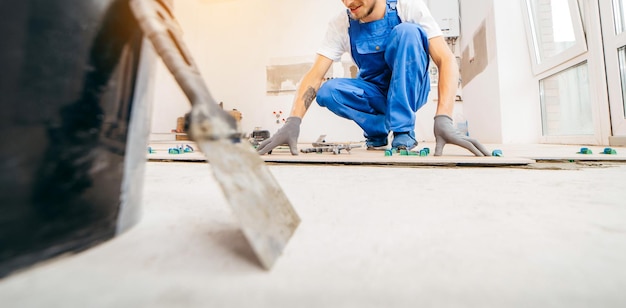 Riparatore adulto in uniforme speciale posa piastrelle con sistema di livellamento piastrelle sul pavimento in una nuova ho