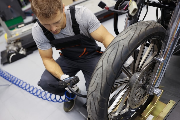 Riparatore dell'uomo che gonfia le gomme del motociclo nel concetto di servizio del motociclo dell'officina riparazioni auto