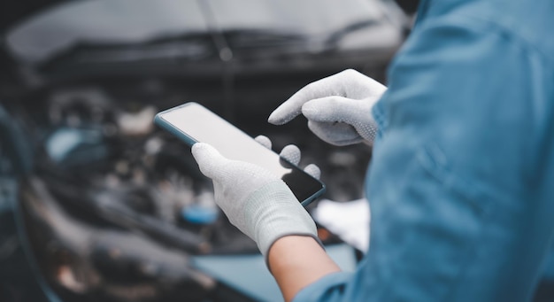 Riparatore esperto che utilizza lo smartphone per diagnosticare i problemi dell'auto in garage Primo piano della mano del meccanico che tiene la chiave mentre esamina il motore Fotografia orizzontale con sfondo dell'officina