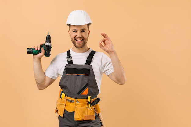 Riparatore maschio positivo a casa che tiene un cacciavite e mostra bene su uno sfondo beige