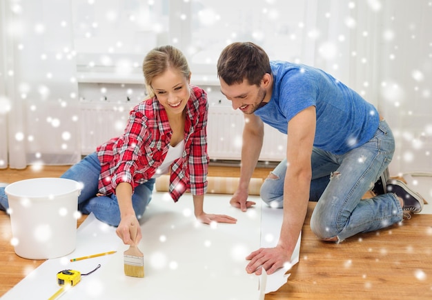 riparazione, costruzione, lavoro di squadra e concetto di casa - coppia sorridente che imbratta la carta da parati con la colla