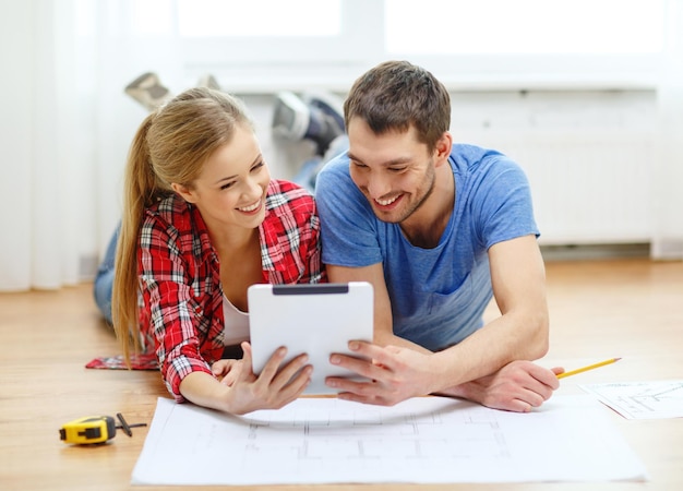 riparazione, costruzione, ristrutturazione e concetto di casa - coppia sorridente guardando tablet pc a casa