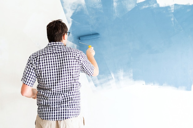 Riparazione e miglioramento della casa. Uomo che colora la parete blu con un rullo