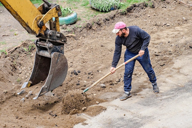 Riparazione e miglioramento della strada e dell'area circostante Tuttofare con la pala che ripara la superficie stradale il giorno d'estate Lavori di riparazione su strada Autentico flusso di lavoro