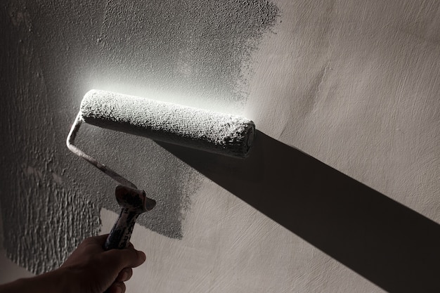 Riparazioni domestiche. Dipingere le pareti della stanza in grigio con un rullo di vernice.