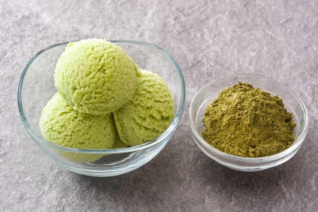 Ripartitori di matcha del tè verde in ciotola a cristallo su pietra grigia